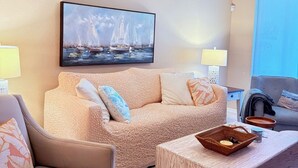 Una sala de estar con un sofá color beige, una mesa de centro de madera y un cuadro de veleros en la pared.