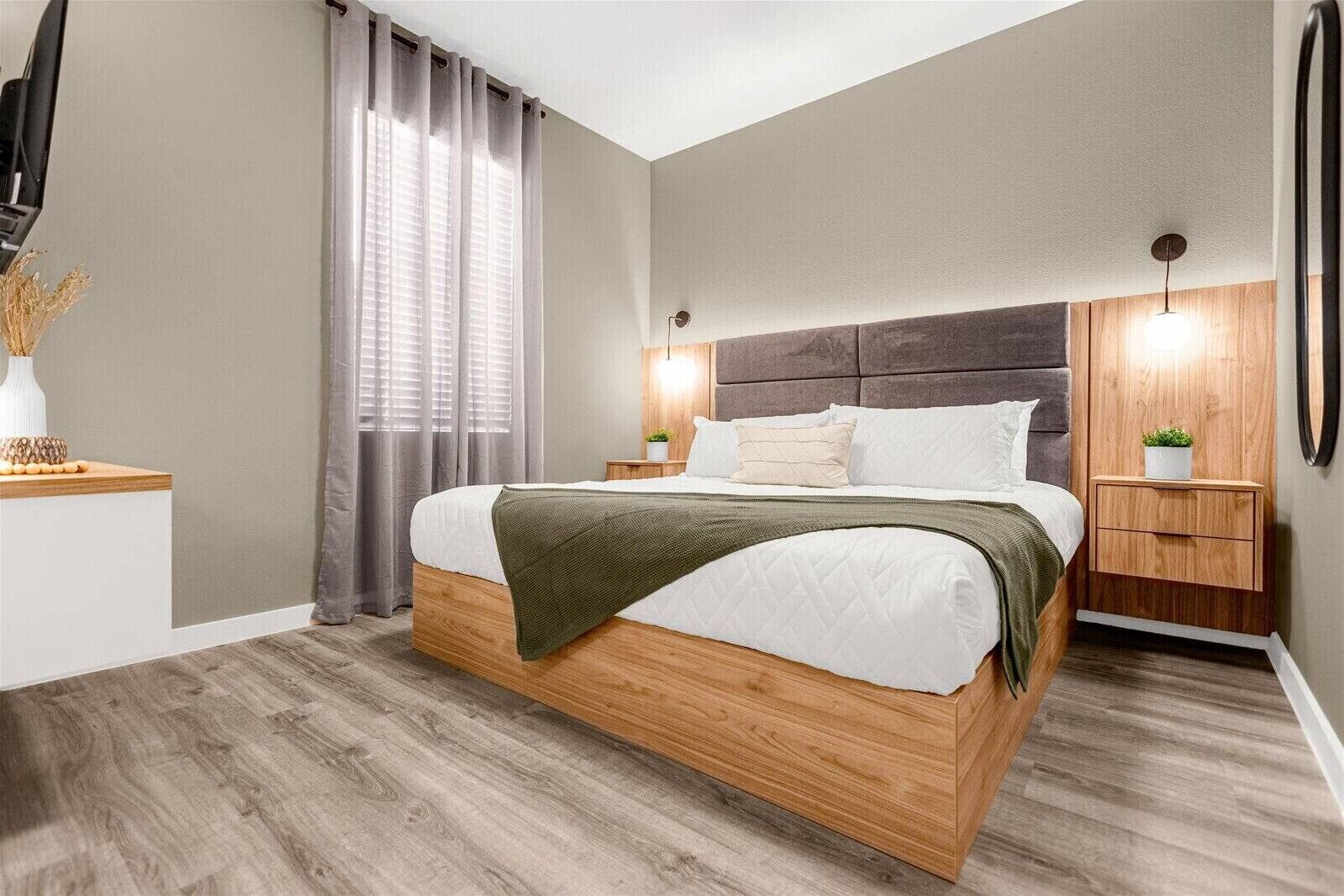 Une chambre moderne avec un lit en bois, des rideaux gris, des tables de chevet avec des lampes et un miroir au mur.