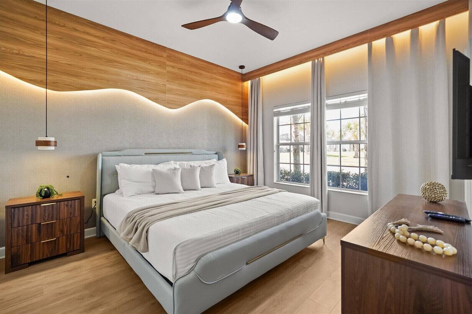 A modern bedroom with a bed, bedside tables, a desk, and a ceiling fan.