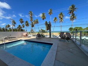 Ein Schwimmbecken mit Liegestühlen und Blick auf den Strand.