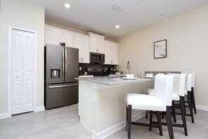 A modern kitchen with white cabinets, stainless steel appliances, and a central island with bar stools. - Last Minute Disney Getaway! Modern Townhouse & Themed Bedrooms. Book Now! #172513 (Orlando)