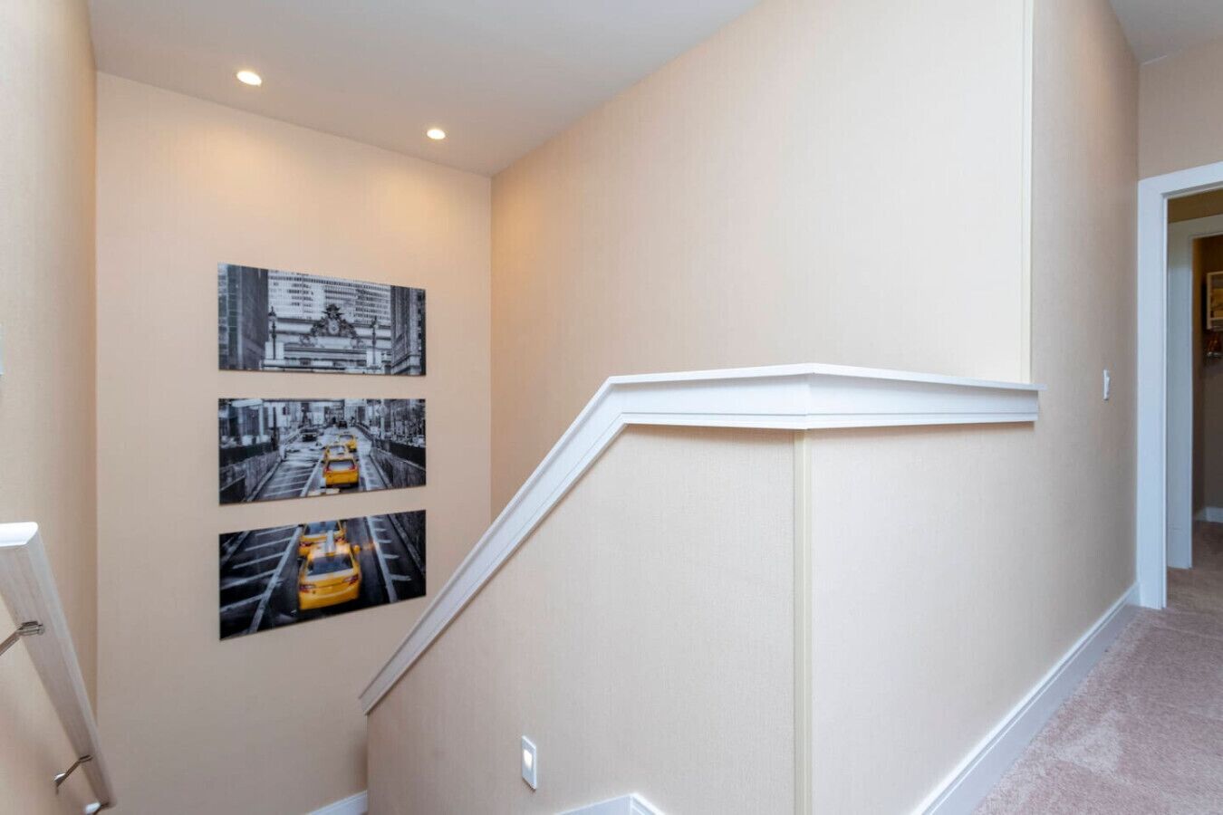 A hallway with beige walls, a white baseboard, and three black and white photographs of city streets.