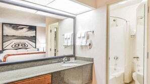 A bathroom with a granite countertop, a sink, a mirror, a shower, and a towel rack. - Super 8 by Wyndham Clovis (Clovis)