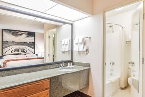 Un baño con encimera de granito, lavamanos, espejo, ducha y toallero.