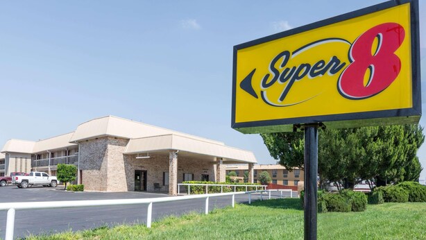 A hotel with a prominent 'Super 8' sign, a parking lot, and a building with a beige facade. - Super 8 by Wyndham Clovis (Clovis)