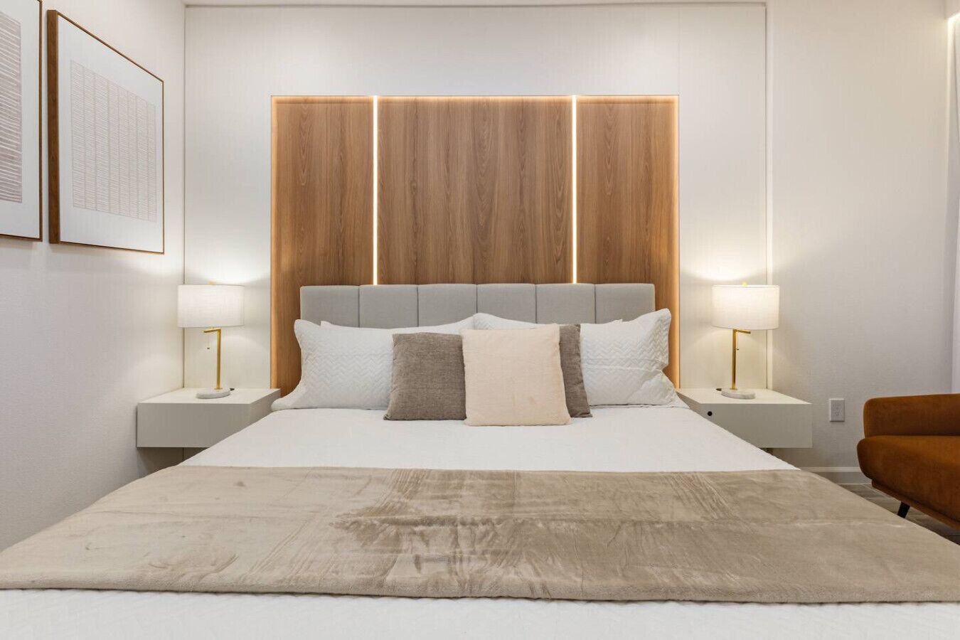 Un dormitorio moderno con una cama grande, dos mesitas de noche, un cabecero con iluminación integrada y un sillón marrón.