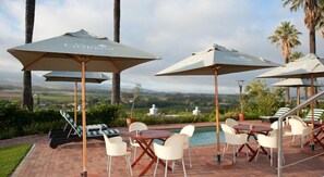 Área à beira da piscina com espreguiçadeiras, guarda-sóis e vista para a paisagem.