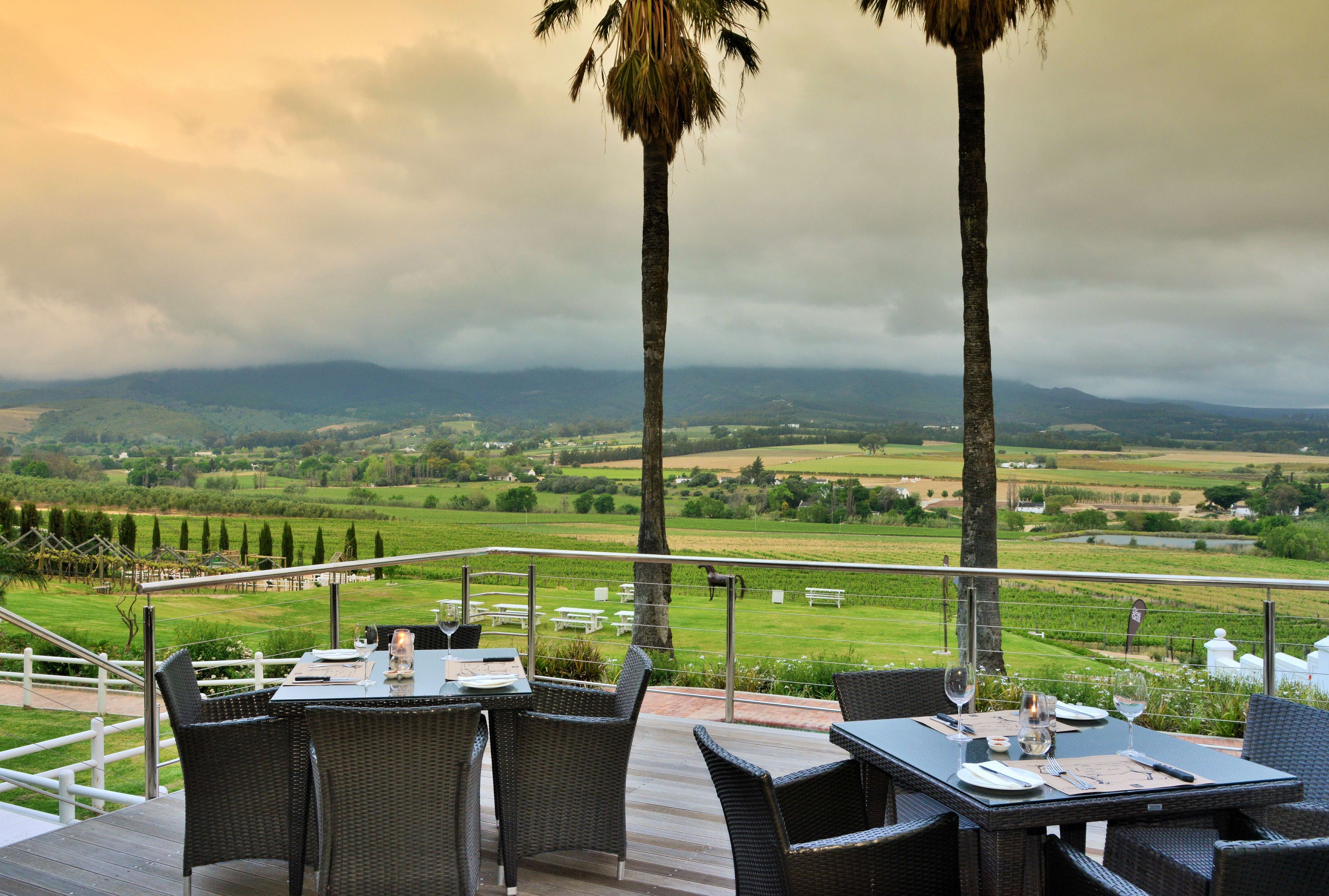 An outdoor dining area with tables and chairs, overlooking a scenic landscape with fields and mountains.