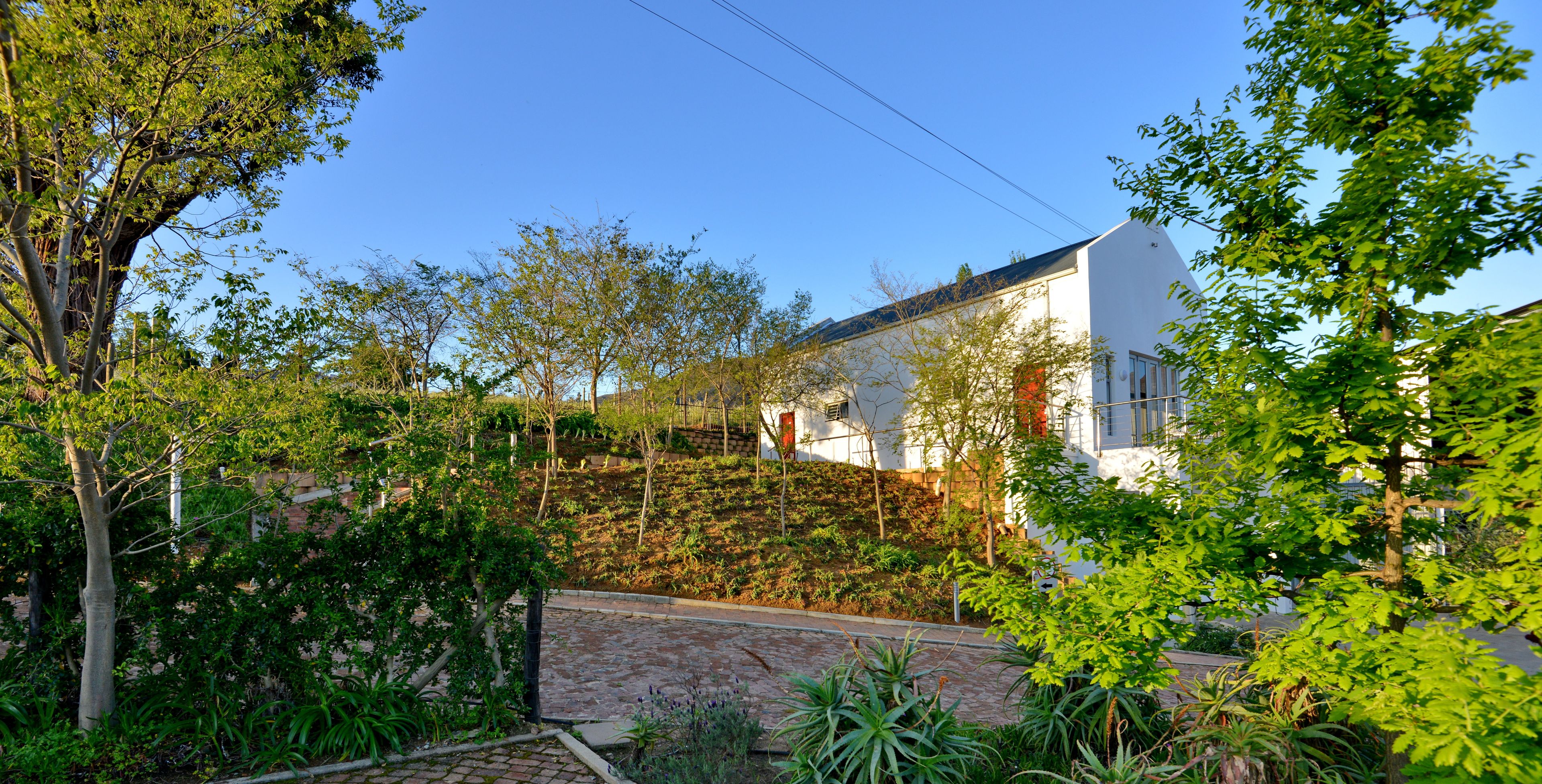 Um edifício branco com telhado inclinado, rodeado por vegetação exuberante e árvores.