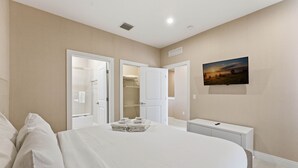 Une chambre à coucher avec un grand lit, un dressing, une table de chevet et un téléviseur fixé au mur.