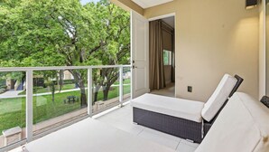 Un balcon avec un canapé blanc, un fauteuil en osier et une vue sur une pelouse verdoyante et des arbres.