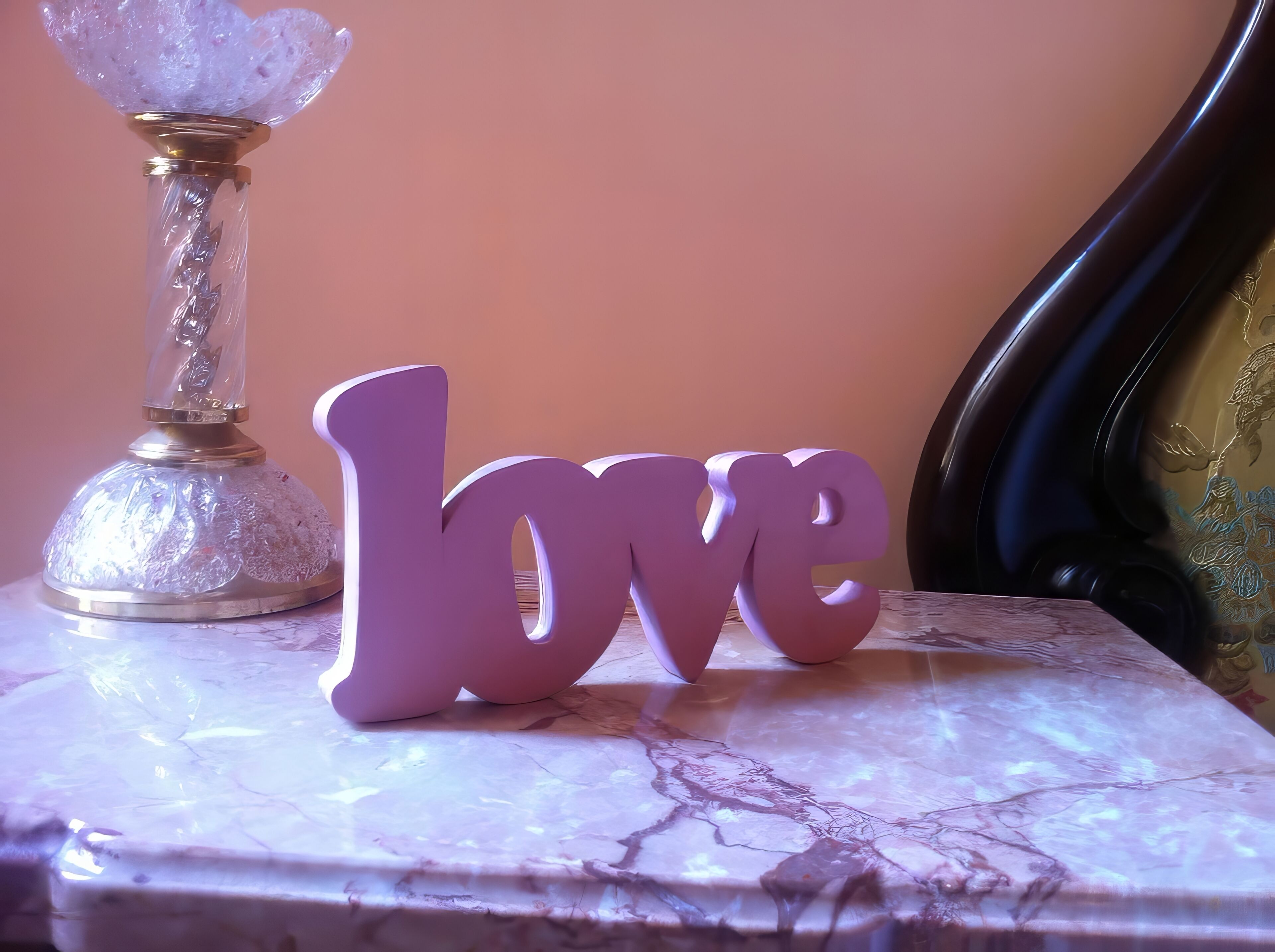 A decorative item spelling 'love' on a marble surface, a crystal vase, and a dark upholstered chair.