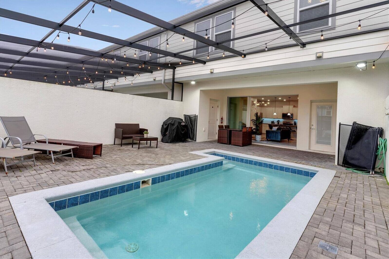 A swimming pool with lounge chairs, a barbecue grill, and a covered patio area.