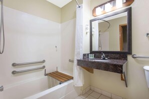 Casa de banho com chuveiro, lavatório, espelho e barras de apoio.