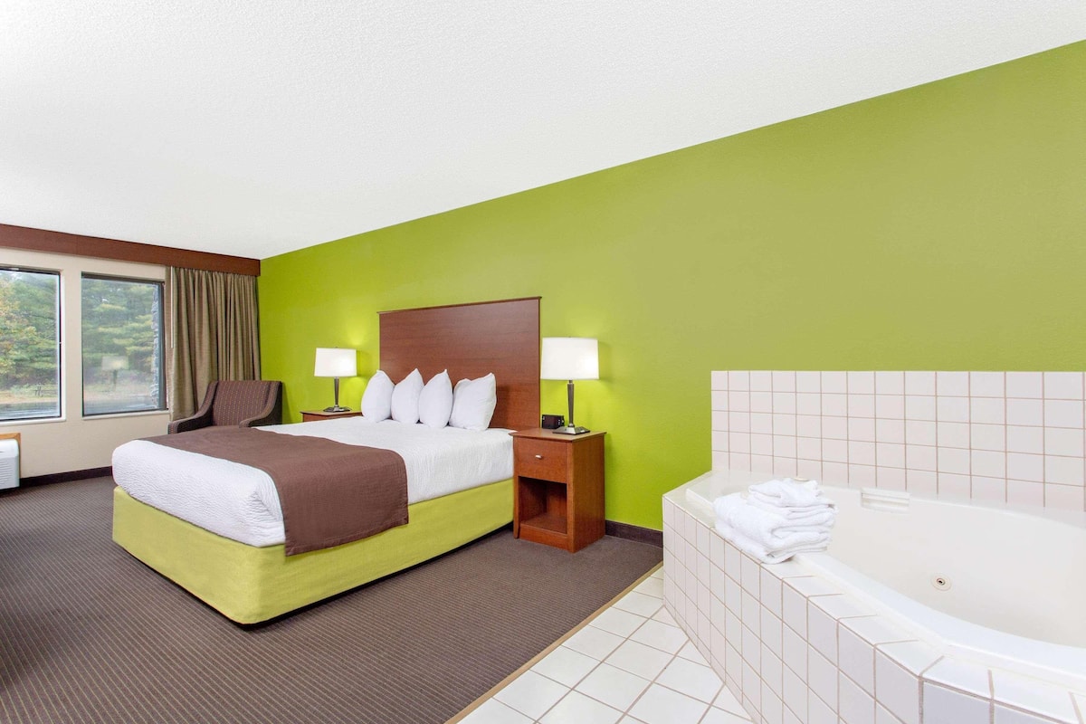 Una habitación de hotel con cama, mesitas de noche, lámpara, ventana y bañera.