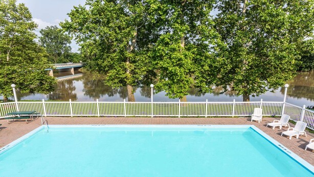 A swimming pool with a white fence, surrounded by trees and a bridge in the background. - Days Inn by Wyndham Tiffin (Tiffin)