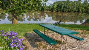 A picnic table with benches, surrounded by a grassy area with purple flowers, near a calm body of water. - Days Inn by Wyndham Tiffin (Tiffin)
