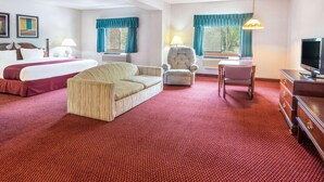 A hotel room with a bed, a sofa, a chair, a desk, a TV, and two windows with curtains. - Days Inn by Wyndham Tiffin (Tiffin)