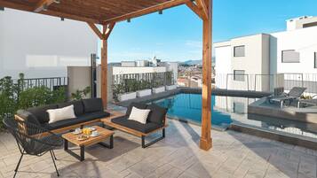 Una terraza en la azotea con piscina, mobiliario exterior y vistas a la ciudad.