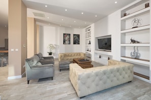 A modern living room with a sofa, two armchairs, a coffee table, and a TV. There are shelves with decorative items and a plant. - Luxury villa Natali with pool (Podstrana)