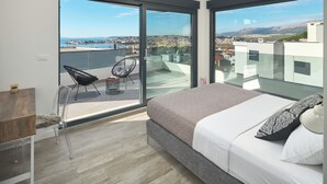 A bedroom with a large bed, a chair, and a view of a cityscape through floor-to-ceiling windows. - Luxury villa Natali with pool (Podstrana)