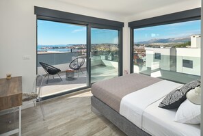 A modern bedroom with a large bed, a chair, and a balcony with a view of the city and mountains. - Luxury villa Natali with pool (Podstrana)