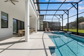 Ein moderner Poolbereich im Freien mit blauem Himmel, überdachter Sitzgelegenheit und Blick auf die umliegende Landschaft.