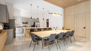 Cozinha moderna com ilha central, luminárias pendentes e área de jantar com mesa grande e cadeiras.