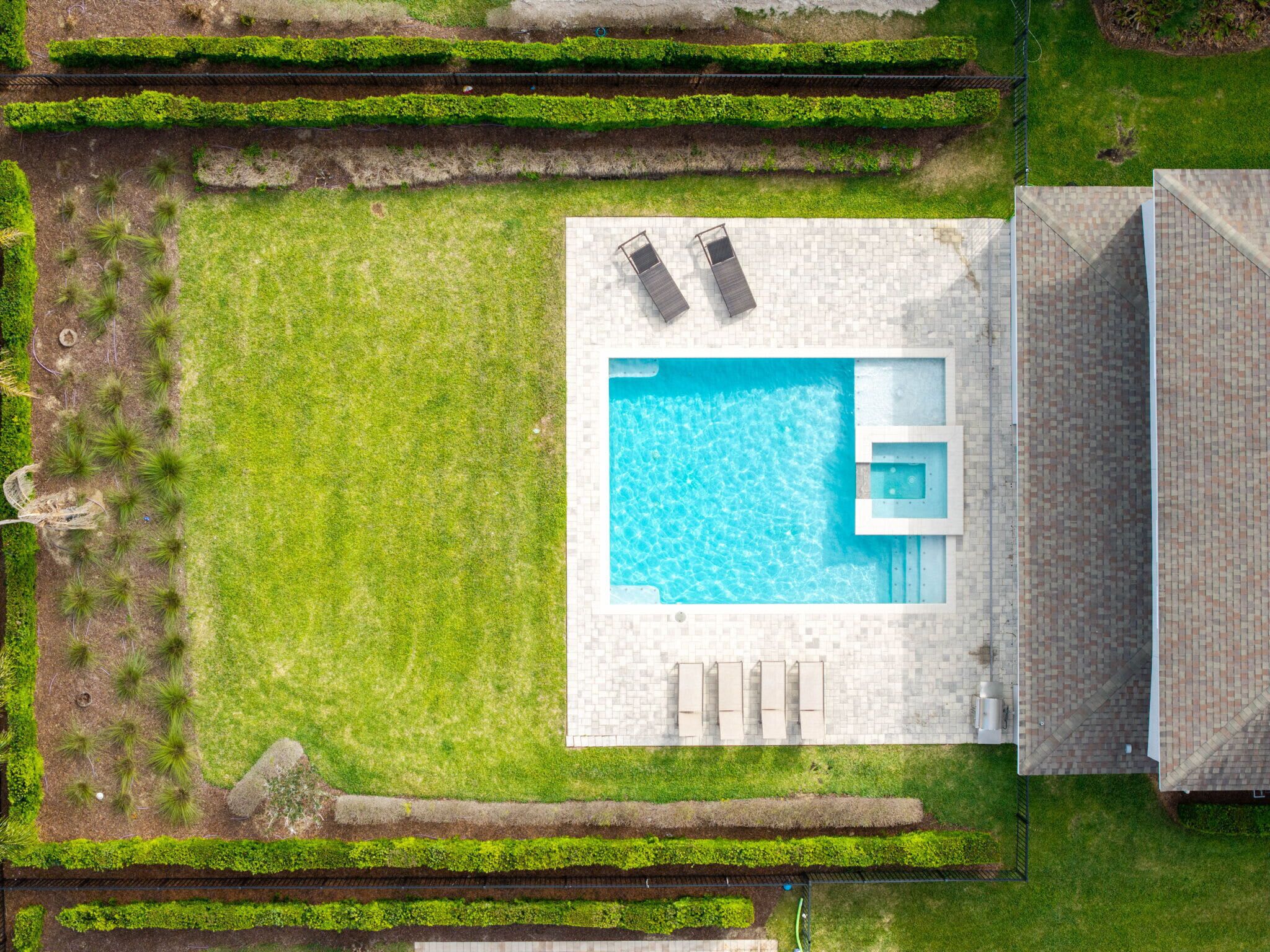 An aerial view of a swimming pool with two lounge chairs, a small jacuzzi, and a paved deck area.