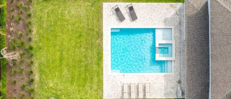 An aerial view of a swimming pool with two lounge chairs, a small jacuzzi, and a paved deck area.