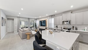 Una cocina moderna con armarios blancos, una isla central y un rincón comedor con sofá y sillas.