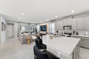 Eine moderne Küche mit weißen Schränken, einer zentralen Kochinsel und einem Essbereich mit einer Couch und Stühlen.