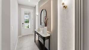 Un pasillo con una puerta, una consola con un florero, un espejo y un aplique de pared.