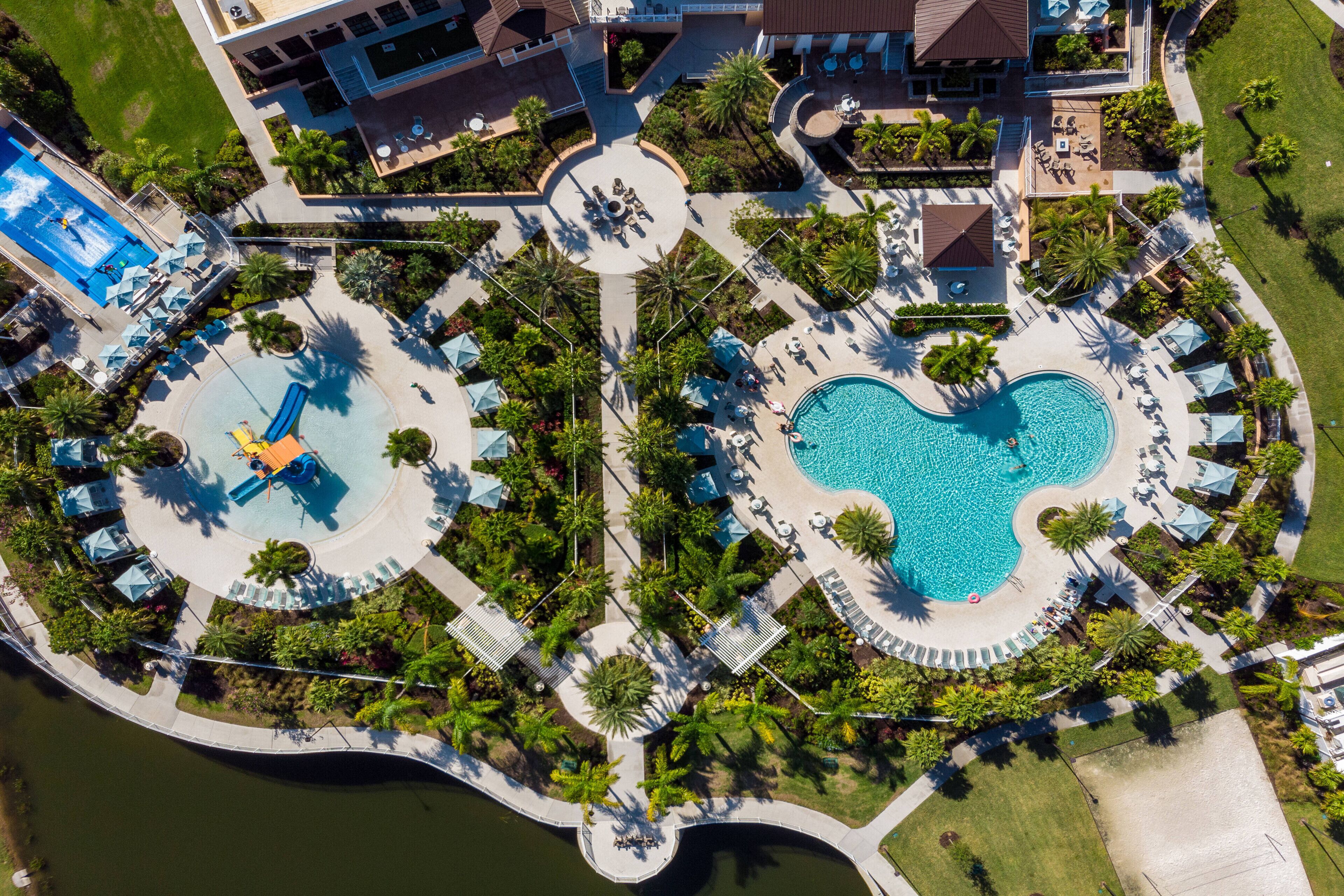 An aerial view of a resort with a central pool, a water slide, and surrounding lounge areas.