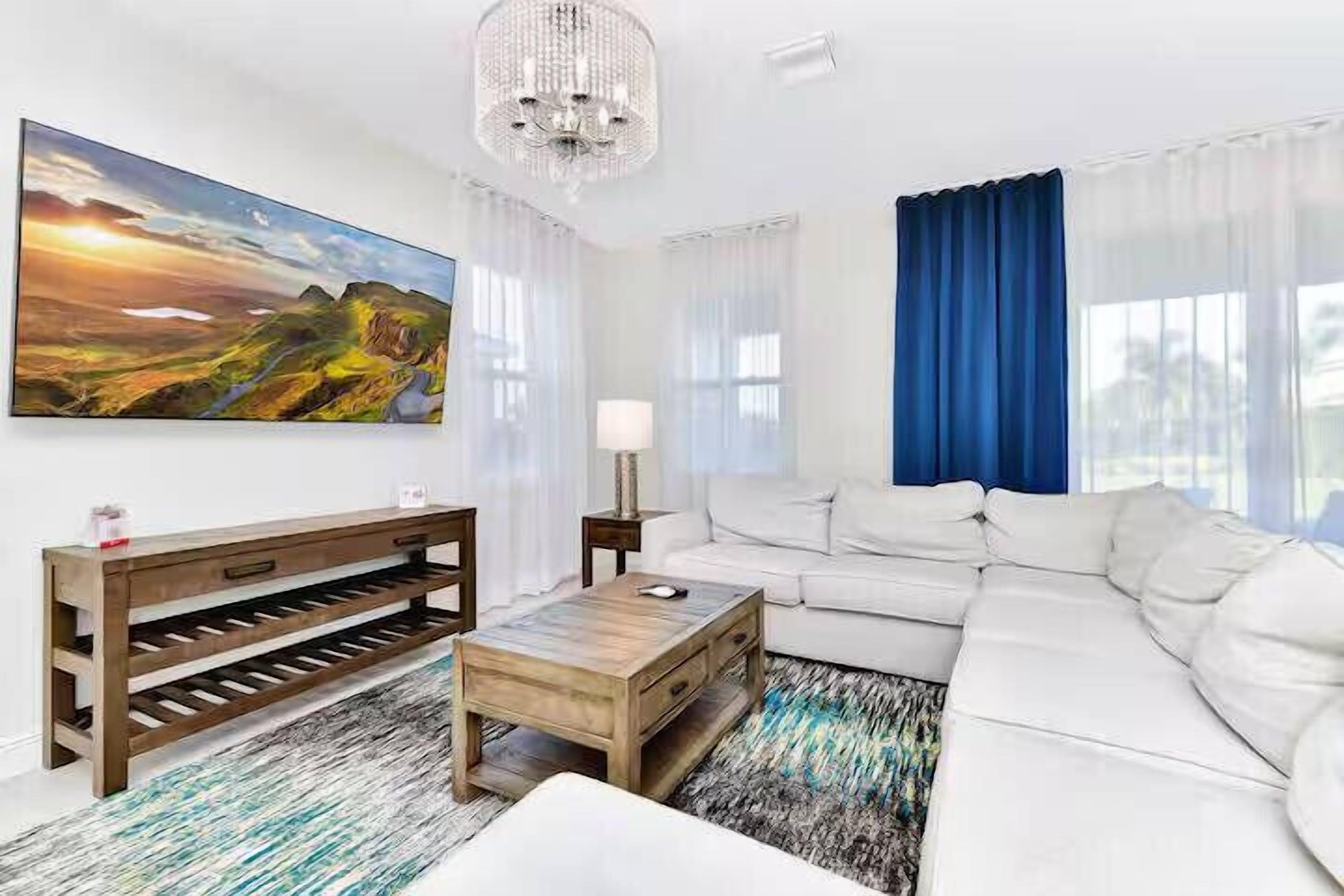 A modern living room with a white sofa, a wooden coffee table, a bench with shelves, a chandelier, and a large landscape painting.