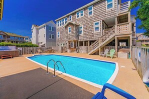 Ein Schwimmbad mit Holzterrasse, einer überdachten Sitzgelegenheit und einem mehrstöckigen Gebäude mit Holzfassade.
