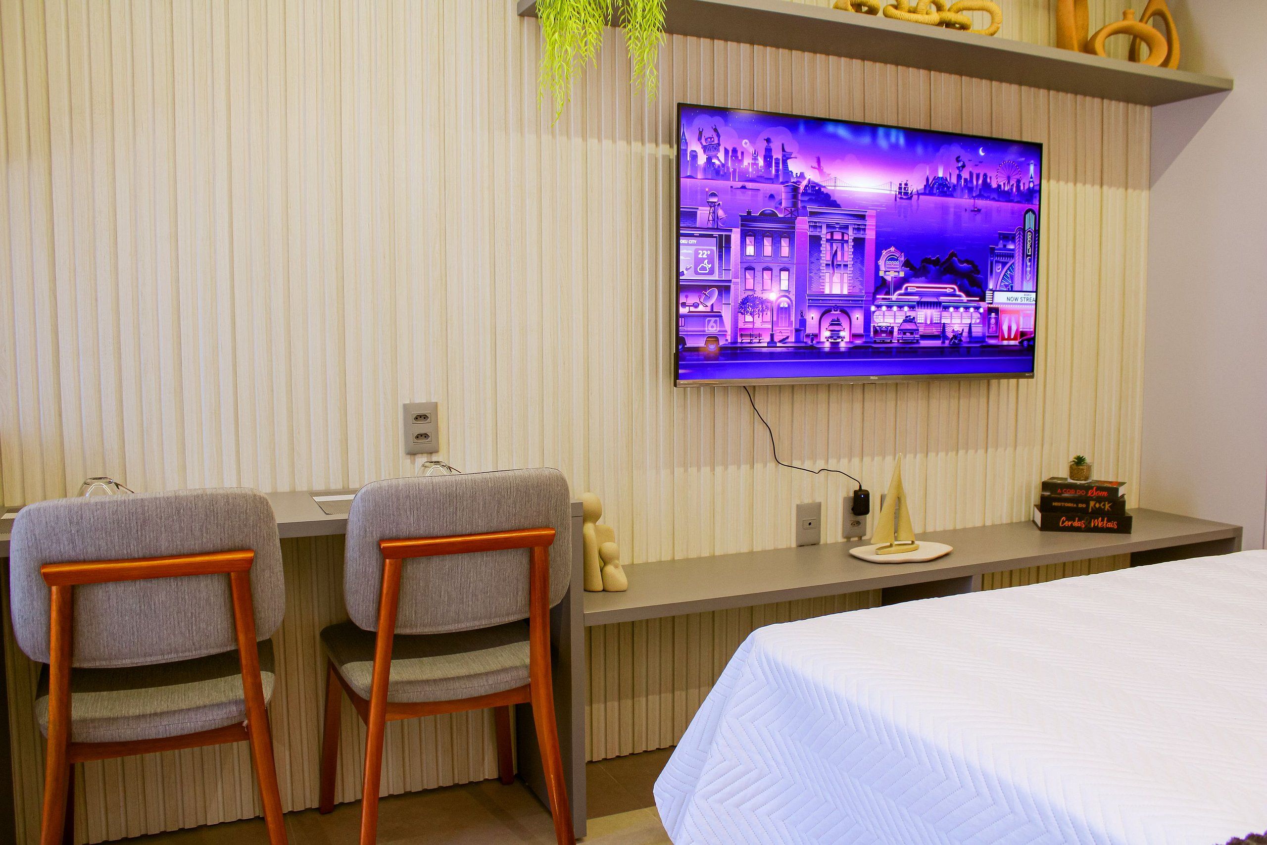Hotelkamer met een televisie aan de muur, twee stoelen, een bed en een tafeltje met decoratieve objecten.