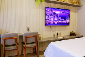A hotel room with a TV on the wall, two chairs, a bed, and a small table with decorative items. - Acqua Tambaú Comfort II - By Almare (João Pessoa)