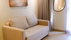 Ein beiges Sofa mit Kissen, ein runder Spiegel und ein Gemälde an der Wand.