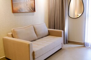 A beige sofa with a cushion, a round mirror, and a painting on the wall. - Acqua Tambaú Comfort II - By Almare (João Pessoa)