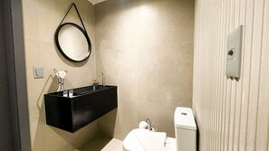 Ein Badezimmer mit einem schwarzen Waschtisch, einem runden Spiegel, einer Toilette und einem Handtuchhalter.