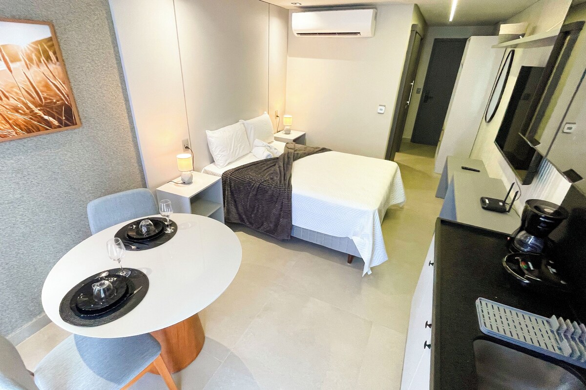 Ein kompaktes Hotelzimmer mit einem Bett, Nachttisch, Lampe und einer kleinen Essecke mit Tisch und Stühlen.