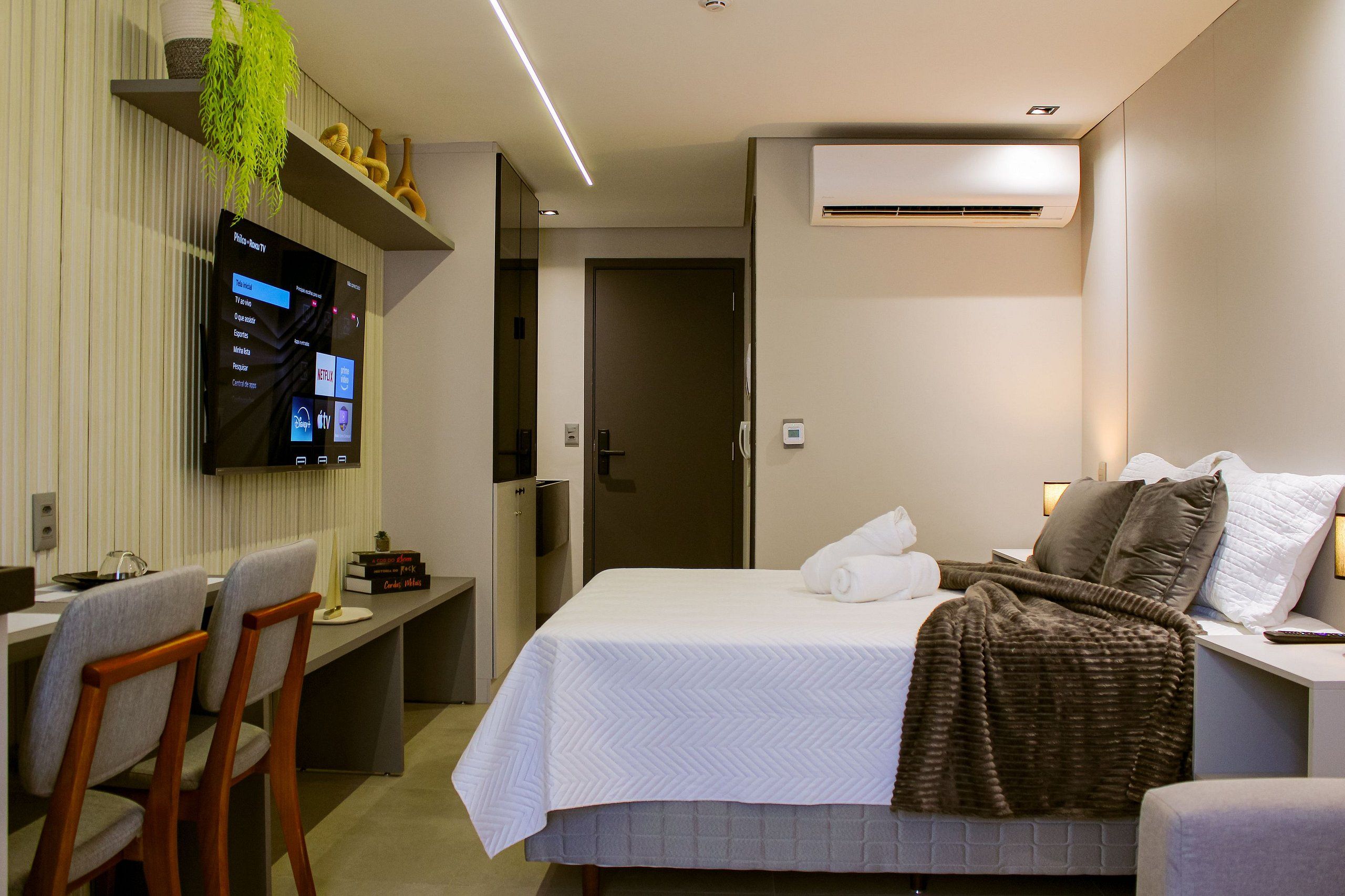 Ein Hotelzimmer mit einem Bett, einem Schreibtisch mit Computer, einem Fernseher und einer Klimaanlage.