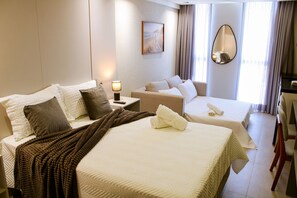 Ein Hotelzimmer mit zwei Betten, einem Schreibtisch, einem Stuhl, einer Lampe, einem Spiegel und einem Bild an der Wand.