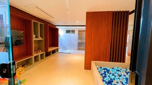 A hallway with wooden shelving, a bench, and a ball pit. - Acqua Tambaú Comfort II - By Almare (João Pessoa)