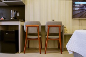 A hotel room with a kitchenette, two wooden chairs, a bed, and a TV displaying a menu. - Acqua Tambaú Comfort II - By Almare (João Pessoa)