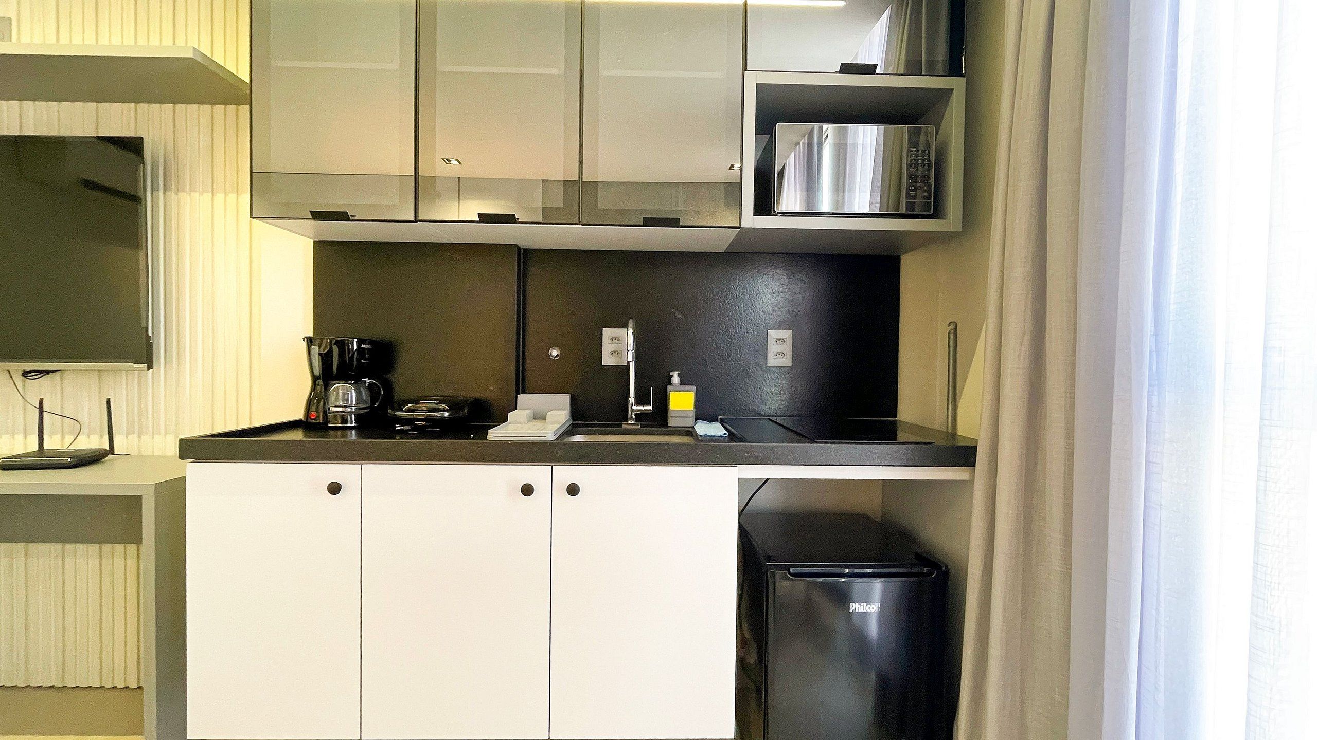 Uma cozinha compacta equipada com micro-ondas, cafeteira e um pequeno frigorífico.