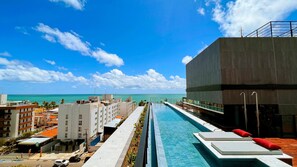 A swimming pool with a view of the ocean, a modern building, and a parking area. - Acqua Tambaú Comfort II - By Almare (João Pessoa)