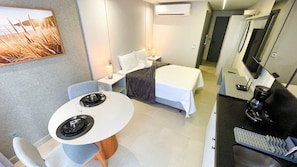 A compact hotel room with a bed, bedside table, lamp, and a small dining area with a table and chairs. - Acqua Tambaú Comfort II - By Almare (João Pessoa)
