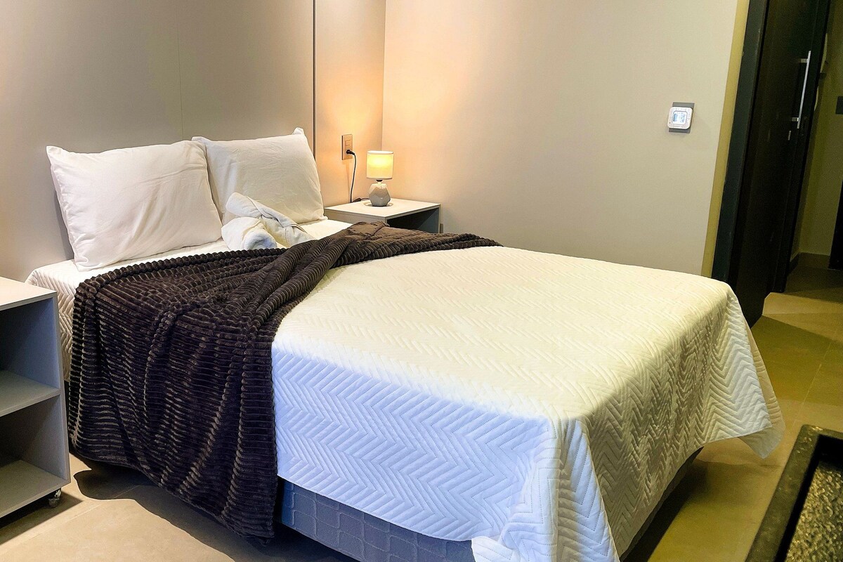 Ein Hotelzimmer mit einem Bett, zwei Nachttischen mit Lampen, einem Beistelltisch und einem an der Wand montierten Lichtschalter.